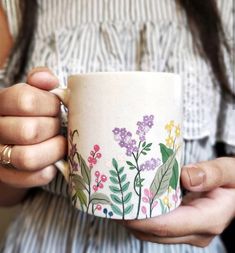 a woman holding a coffee cup with flowers painted on it