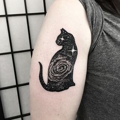 a black cat tattoo on the left upper arm with stars and galaxy in the background