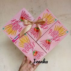 a hand holding up two pink boxes with strawberries on them and gold ribbon around the top