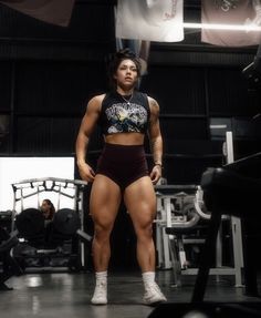 a woman in a black top and shorts standing on a gym floor with her hands behind her back