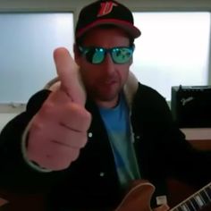 a man wearing sunglasses and a hat gives the thumbs up sign while holding an electric guitar