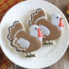 two decorated turkey cookies sitting on top of a white plate next to an orange and yellow plaid table cloth