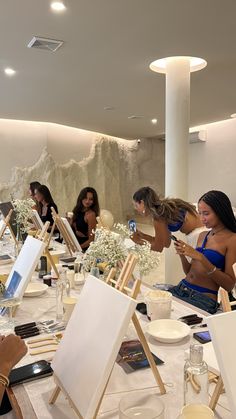 a group of women sitting around a table with easels and paintings on the tables