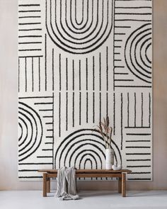 a white and black wall hanging over a wooden bench next to a vase with flowers