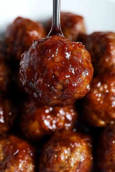 a close up of meatballs being held by a fork with sauce on them and the meatball is covered in ketchup