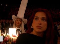 two women sitting at a table with candles in front of them and one woman wearing a white hat