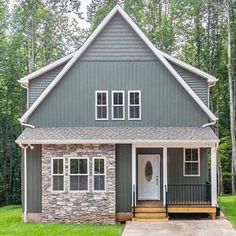 a gray house with white trim and stone accents in the front yard is surrounded by trees