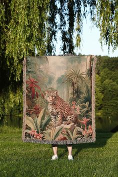 a woman standing in the grass holding up a blanket with a painting of a leopard on it