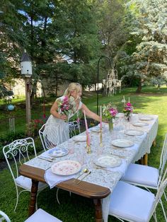 the woman is setting the table outside with flowers in vases and plates on it