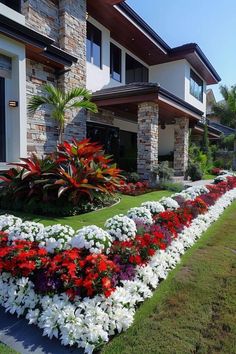 a flower bed in front of a house with white and red flowers on the grass