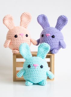 two crocheted rabbits sitting next to each other in front of a wooden crate