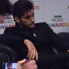 a man sitting in a chair holding a cell phone and looking at his wrist watch