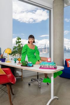 a woman sitting at a desk in front of a window with the city skyline behind her