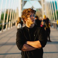 a man standing on a bridge with his arms crossed and people walking across the bridge behind him