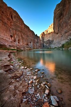 a river with rocks and water in the middle of some mountains at sunset or dawn