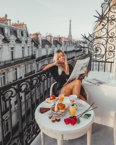 a woman sitting on a balcony reading a newspaper and eating breakfast with her feet up