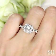 a woman's hand with a diamond ring on top of her finger and flowers in the background