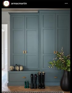 a vase with flowers and rain boots on the floor next to some blue cupboards