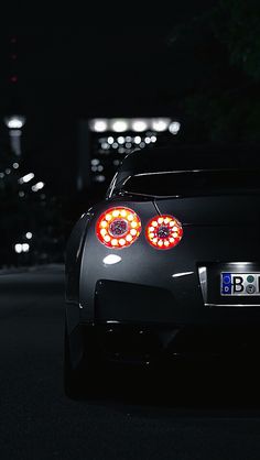 the back end of a black sports car with red lights on it's headlights