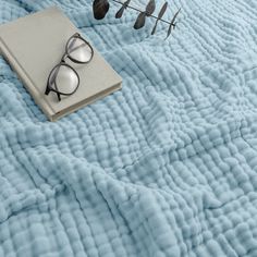 an open book and pair of glasses on top of a blue quilted bedspread