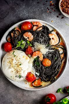 a white plate topped with pasta and shrimp next to tomatoes, sauce and seasoning