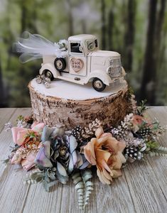 a wedding cake decorated with flowers and an old truck on top of a tree stump