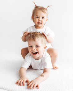 two toddlers are sitting on the floor and one is brushing his hair while the other smiles