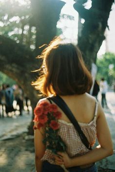 a woman standing next to a tree with flowers in her hand