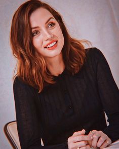 a woman sitting at a table in front of a white wall with a smile on her face