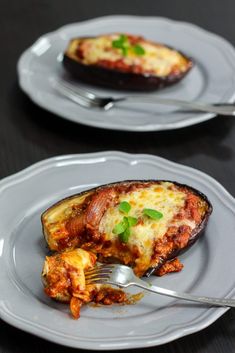 an eggplant stuffed with meat and cheese is served on two white plates, along with a fork