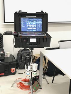 a camera set up in front of a projector screen on a tripod with other equipment around it