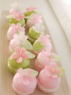 some pink and green cupcakes are on a wooden tray with flowers in them