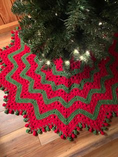 a crocheted christmas tree skirt is on the floor next to a fir tree