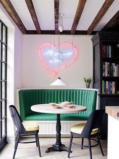 a table with two chairs in front of it and a neon heart sign above the table