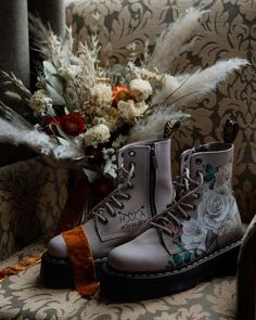 a pair of white boots sitting on top of a chair next to a bouquet of flowers