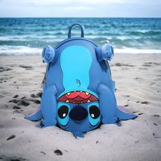 a blue backpack sitting on top of a sandy beach next to the ocean with an alien face painted on it