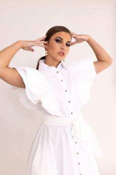 a woman wearing a white dress and holding her hands behind her head while posing for the camera