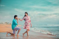 a man kneeling down next to a woman on top of a beach near the ocean