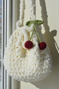 a crocheted bag hanging on the side of a window sill with two cherries attached to it