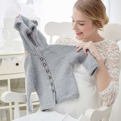 a woman sitting in a chair holding up a knitted sweater with buttons on it