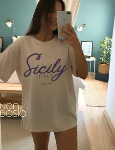 a woman taking a selfie with her cell phone in front of her face and wearing a t - shirt that says scally italy