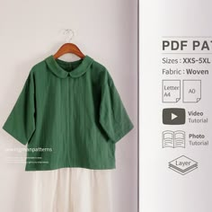 a green shirt hanging on a white wall next to a wooden hanger with an open book