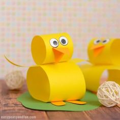 two yellow paper ducks sitting on top of a wooden table next to balls of yarn