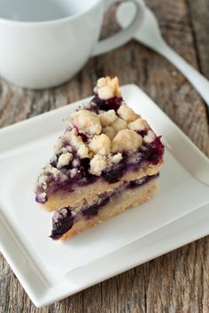 a piece of cake sitting on top of a white plate next to a cup of coffee