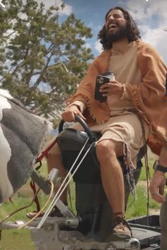 two men sitting on top of a horse in the grass and one is holding a cell phone