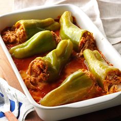 a casserole dish filled with green peppers and meat in tomato sauce on a wooden table