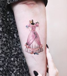 a woman's arm with a pink dress and tiara tattoo on her left arm