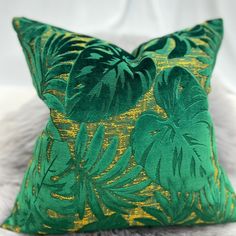 a green and gold pillow on a white furnishing with large leafy leaves