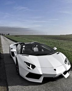 a white sports car parked on the side of a road next to an open field