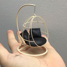 a hand holding a miniature black hat in a white wire birdcage ornament